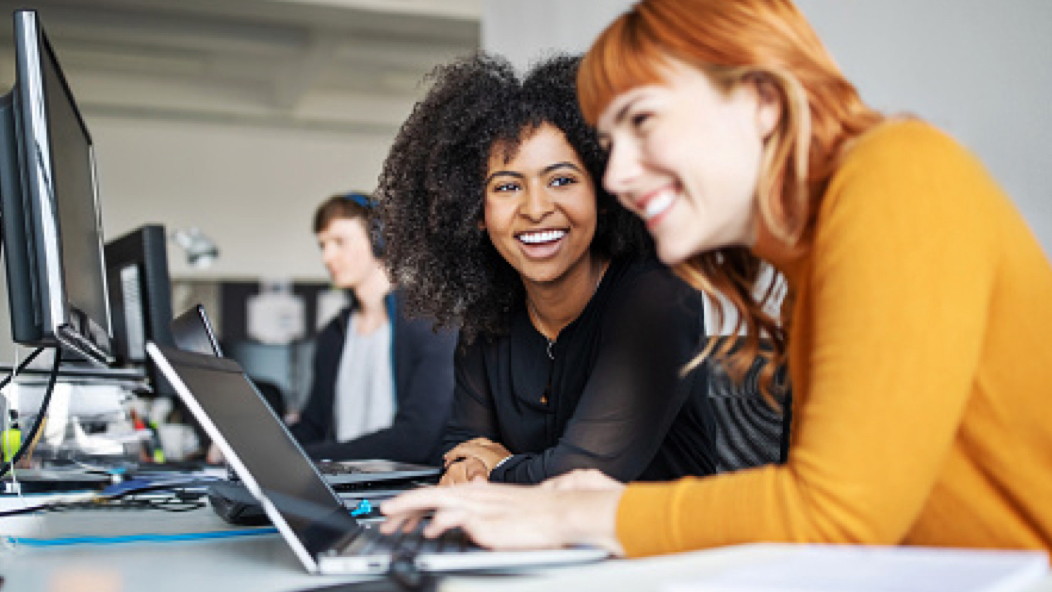 Two women sitting in front of computers, symbolizing Vanguard’s strong corporate culture which includes the highest standards of ethical behavior and demands that all crew place our clients’ interest first.